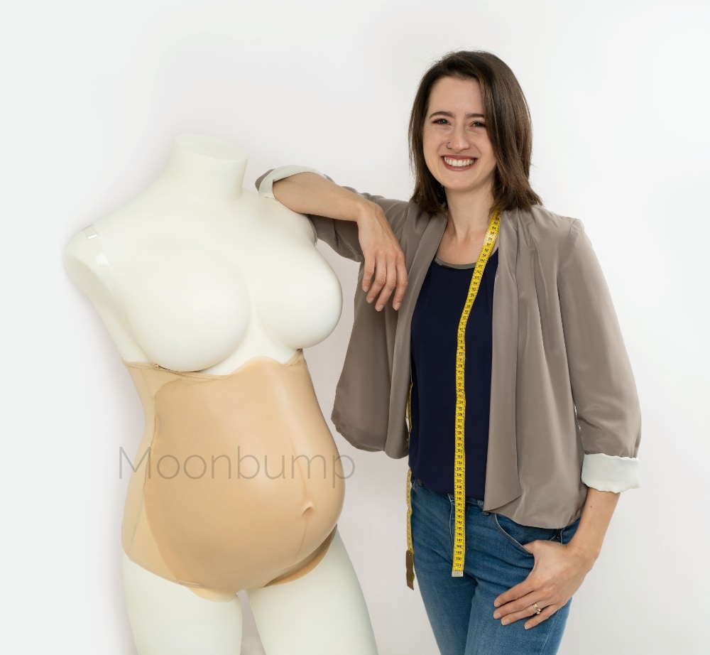 portrait of a woman standing next to a fake pregnant belly on a mannequin